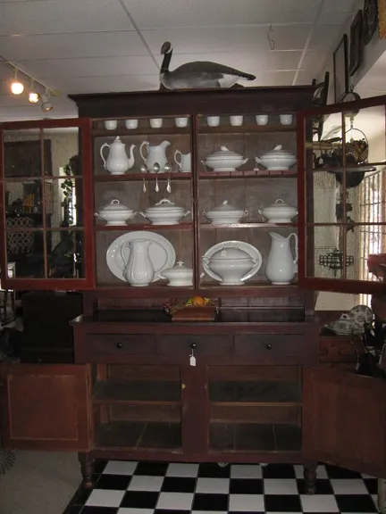 Early 19th Century Cherry Ohio River Valley Cupboard. Two-piece, step-back in original surface, top consisting of two 6-pane doors with original glass. Brass and porcelain catches, simple cove molded crown,
interior fitted with spoon rack, plate rails and top cup shelf. Base consisting of three hand-dovetailed drawers over two hand-chamfered panel doors culminating in turned feet.